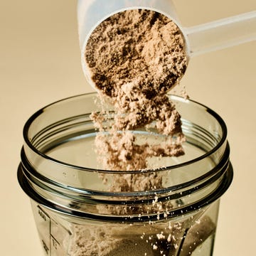 Scoop pouring protein powder into a blender. Scoop pouring protein powder into a blender.