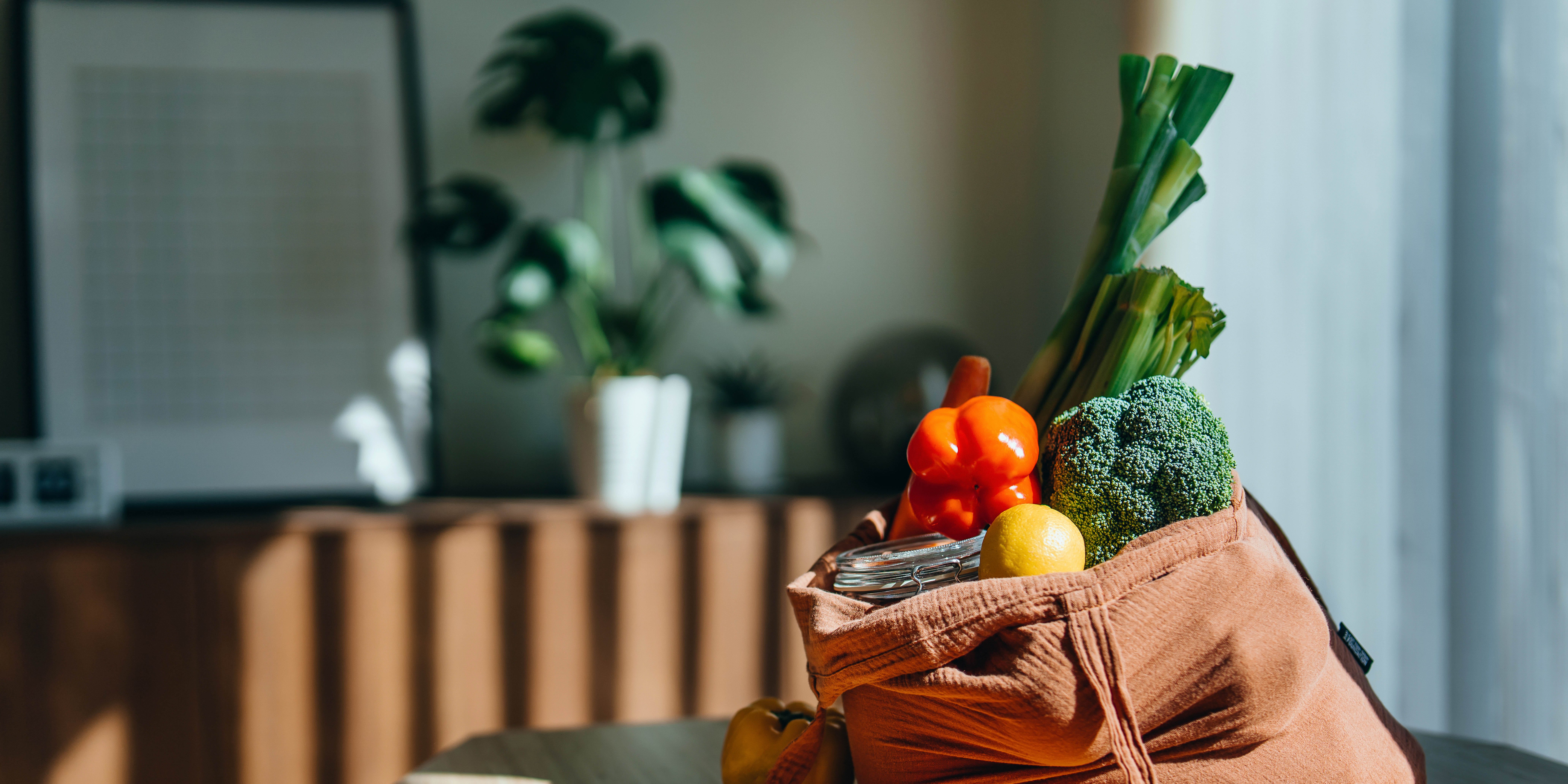 Shopping bag with bright fruits and vegetables eco friendly reusable shopping bag with multi coloured fresh vegetables and groceries on the table at home. shopping with reusable grocery bag