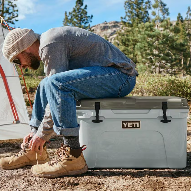 Person sitting on a cooler while tying shoelaces outdoors