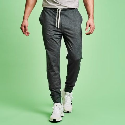 Male model wearing gray joggers and white sneakers against a green background. Male model wearing gray joggers and white sneakers against a green background.