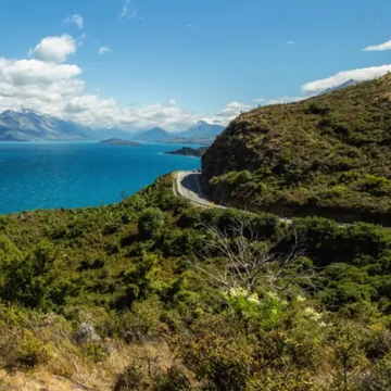 scenic view of a mountainous landscape by a lake with a winding road scenic view of a mountainous landscape by a lake with a winding road
